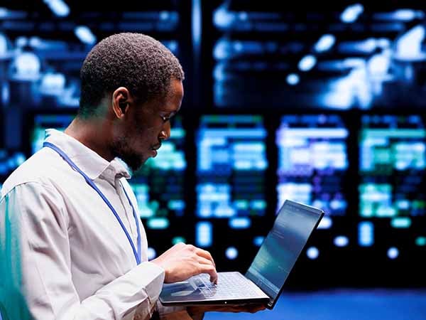 A data center server manager on laptop with monitors in background.