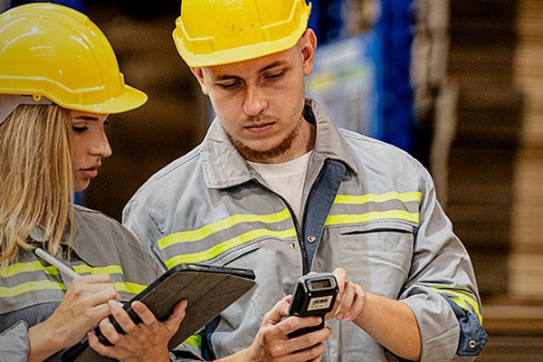 Two workers in hardhats compare notes on digital devices.