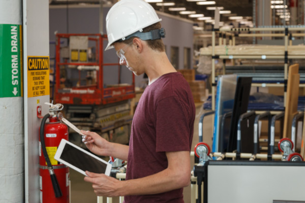 Person in a white hard hat inspecting a fire extinguisher. 