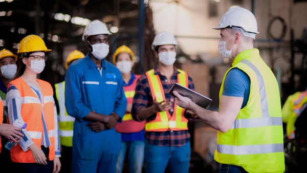 Manager leads group of workers in hardhats through a safety training program.