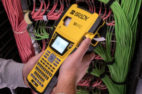 Person holding a Brady M410 printer in front of an organized and labeled server rack.