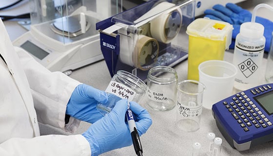 Lab worker writing a handwritten label on clear container.