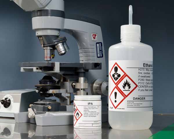 Closeup of a microscope and bottles that have hazard labels on them.