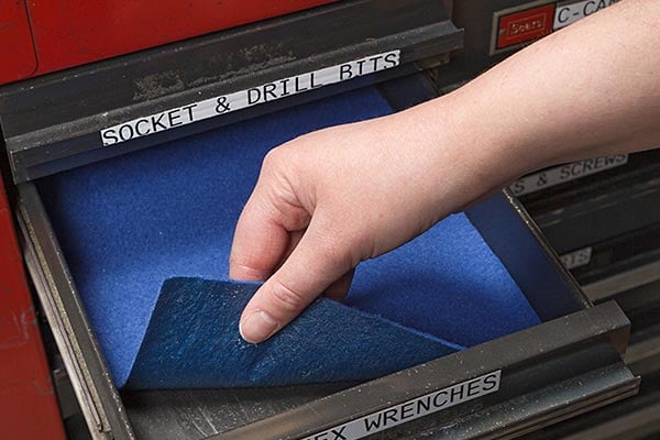 Hand pulling back blue felt lining in a labeled industrial drawer. 