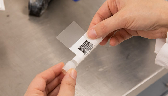 A worker attaches an adhesive barcode label to a vial. 