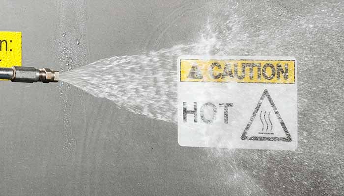A &quot;hot&quot; caution label on a metallic surface is sprayed with liquid.