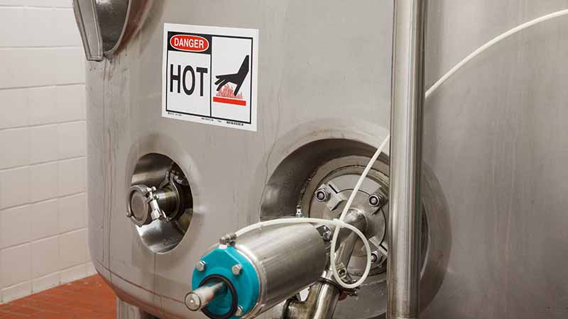 Large stainless steel industrial container with &quot;Caution Hot&quot; warning label.