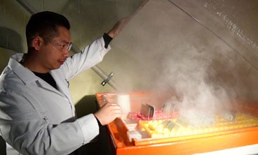 A lab tech applies steam heat to a yellow tray of vials.