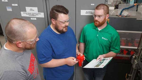 Three men review LOTO procedures while holding a valve lockout device.