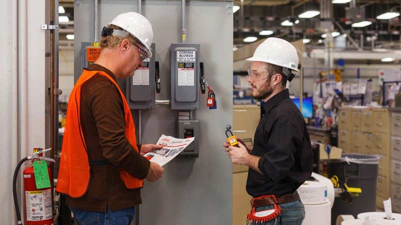Two workers review LOTO procedures in front of an electrical panel.