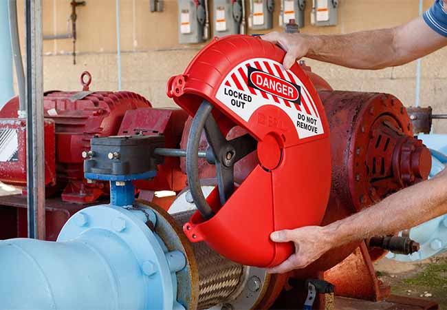 Hands install red LOTO device on a valve handle in an industrial setting.
