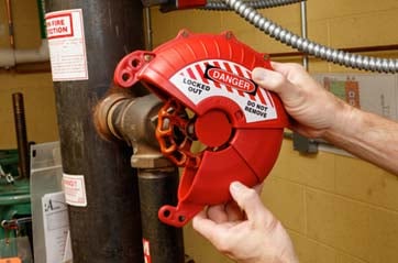Hands attaching a red lockout device to a metal pipe. 
