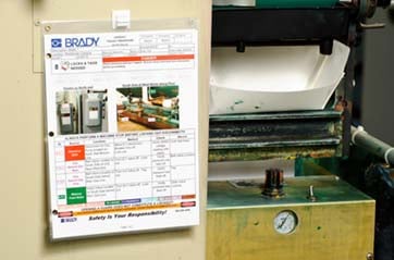 Document in a plastic sleeve attached to a wall near equipment.