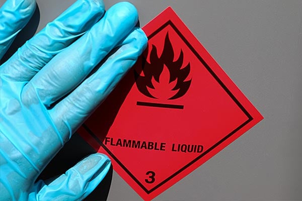 Red flammable hazard sign being placed on a metal container. 