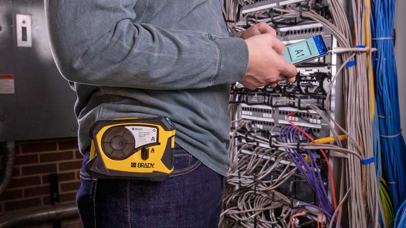  Worker stands next to cables while wearing Brady label printer.