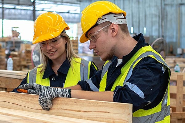 Two workers inspect lumber in a warehouse. 