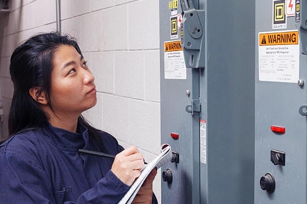 Worker with a clipboard inspecting three electrical panels.