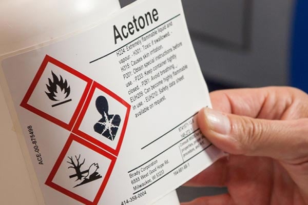 Worker applies a warning label to a bottle of acetone.