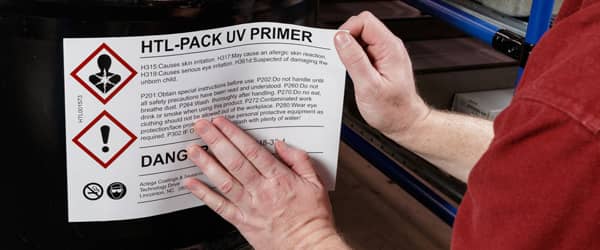 A worker applies large warning label to container of UV primer.