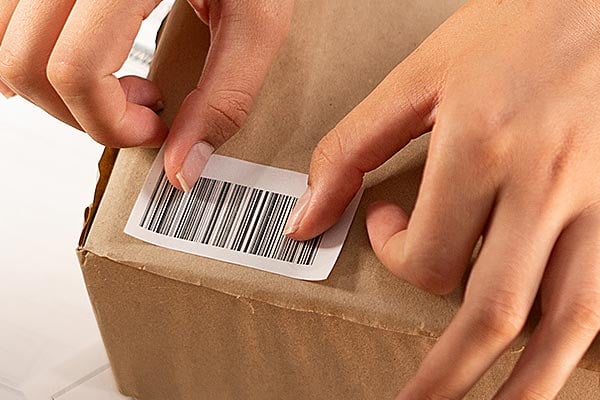 Two hands apply a barcode label on a cardboard box.