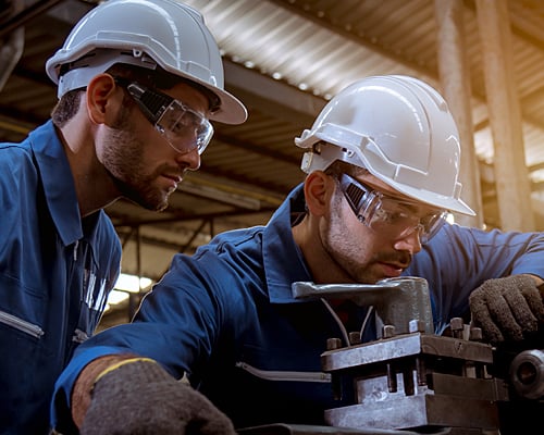 Two workers in safety gear inspect a piece of machinery.