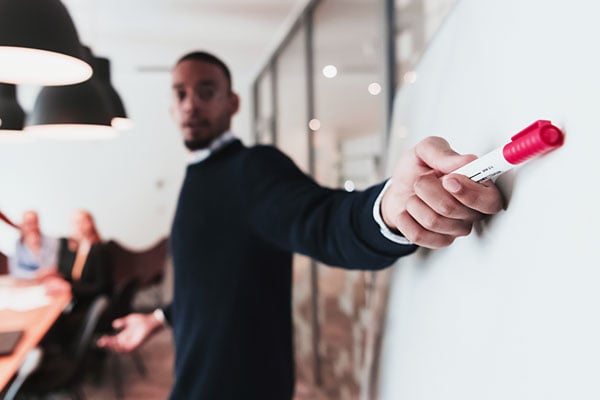 Corporate trainer points to a whiteboard while teaching a class.