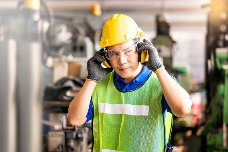 A worker puts on protective hearing covering inside a factory.
