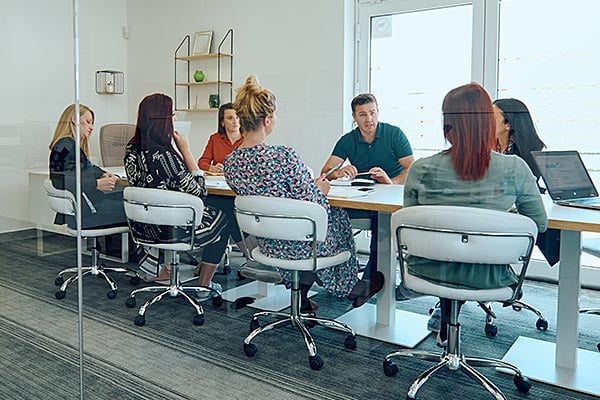 Eight corporate employees sit at long conference table.