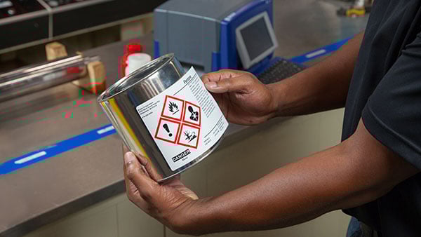 Tech applies a warning label to a silver can.  