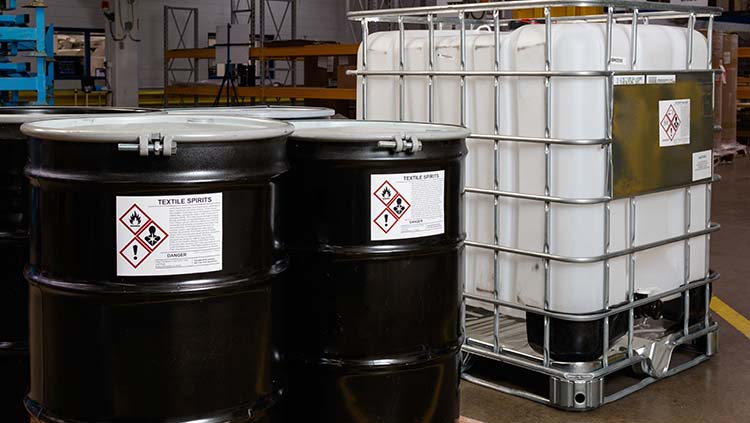 Two black drums, one white vat all with warning labels.