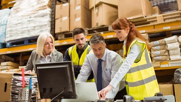 Warehouse managers collaborate around a computer monitor. 