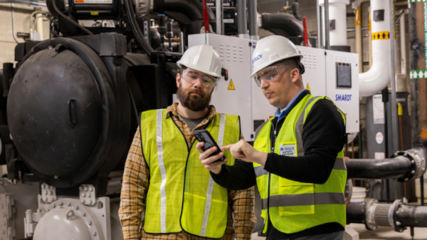Two people in hard hats and safety vests reviewing safety protocols in a manufacturing environment.