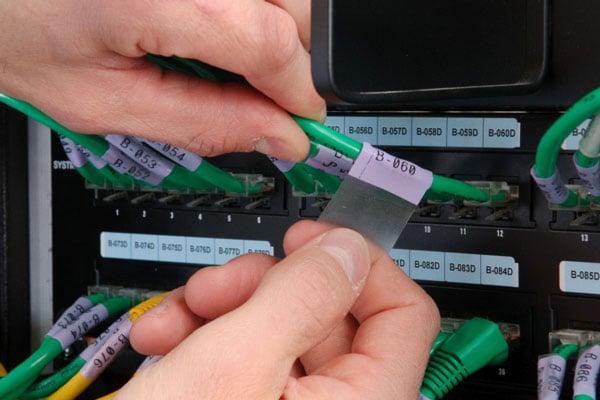 A datacom worker attaching a Brady self-laminating label to a data cable.