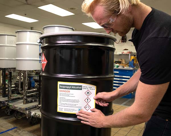 A man applies label to a black barrel in a warehouse. 