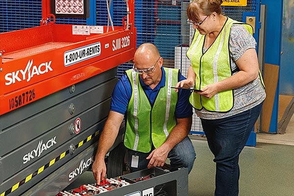 Two employees inspect the battery of a scissor lift.