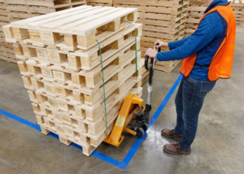 Employee in a safety vest moving wooden pallets with a pallet jack.