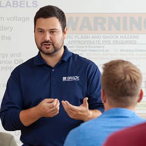 Employee instructs students with warning labels projected behind.