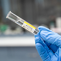 A hand holds a glass vial with a label wrapped around it.