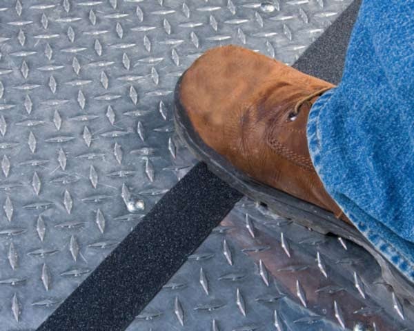 A person stepping on black anti-slip tape applied to a galvanized metal floor.