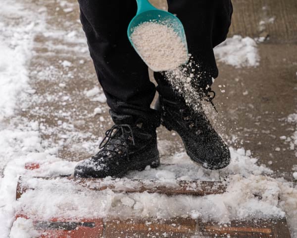 Rock salt being applied to a snowy sidewalk.