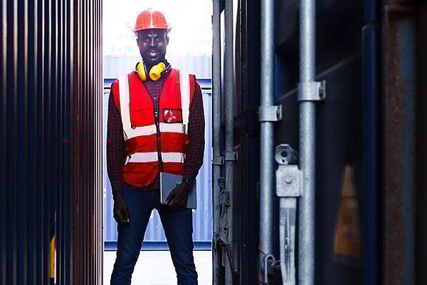 Employee in safety gear surrounded by shipping containers.