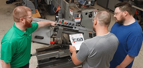 A worker reviewing a lockout procedure with two others in front of the equipment.