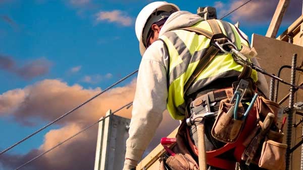 A construction worker wearing a tool belt and harness working on a building.