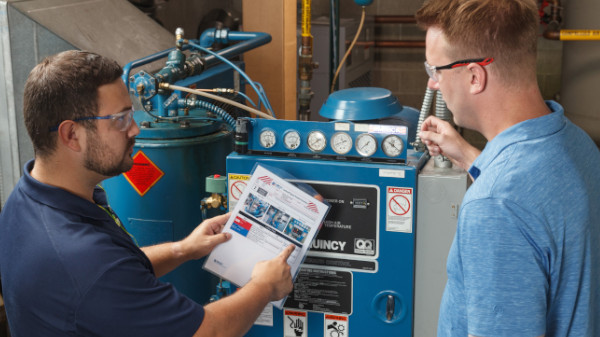 Two people reviewing the lockout procedure for an industrial air compressor.