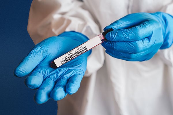 A barcode label on a laboratory vial held by someone with gloves on.
