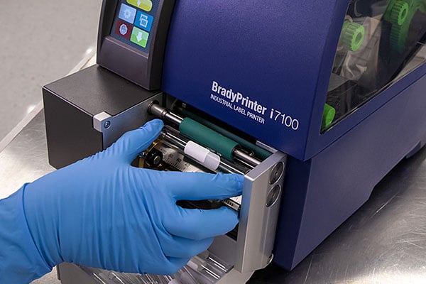 A lab worker loading a vial into a BradyPrinter i7100 label printer.