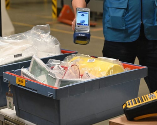 A warehouse worker using a scanner on bin of barcoded objects.