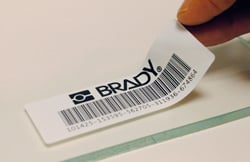 Hand applying a Brady label to a clear slide. 
