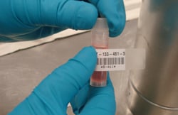 Barcode label on a vial containing pink liquid, in a lab.