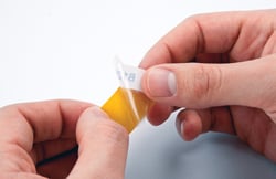 Hands peeling off self-laminating vinyl wrap around labels.